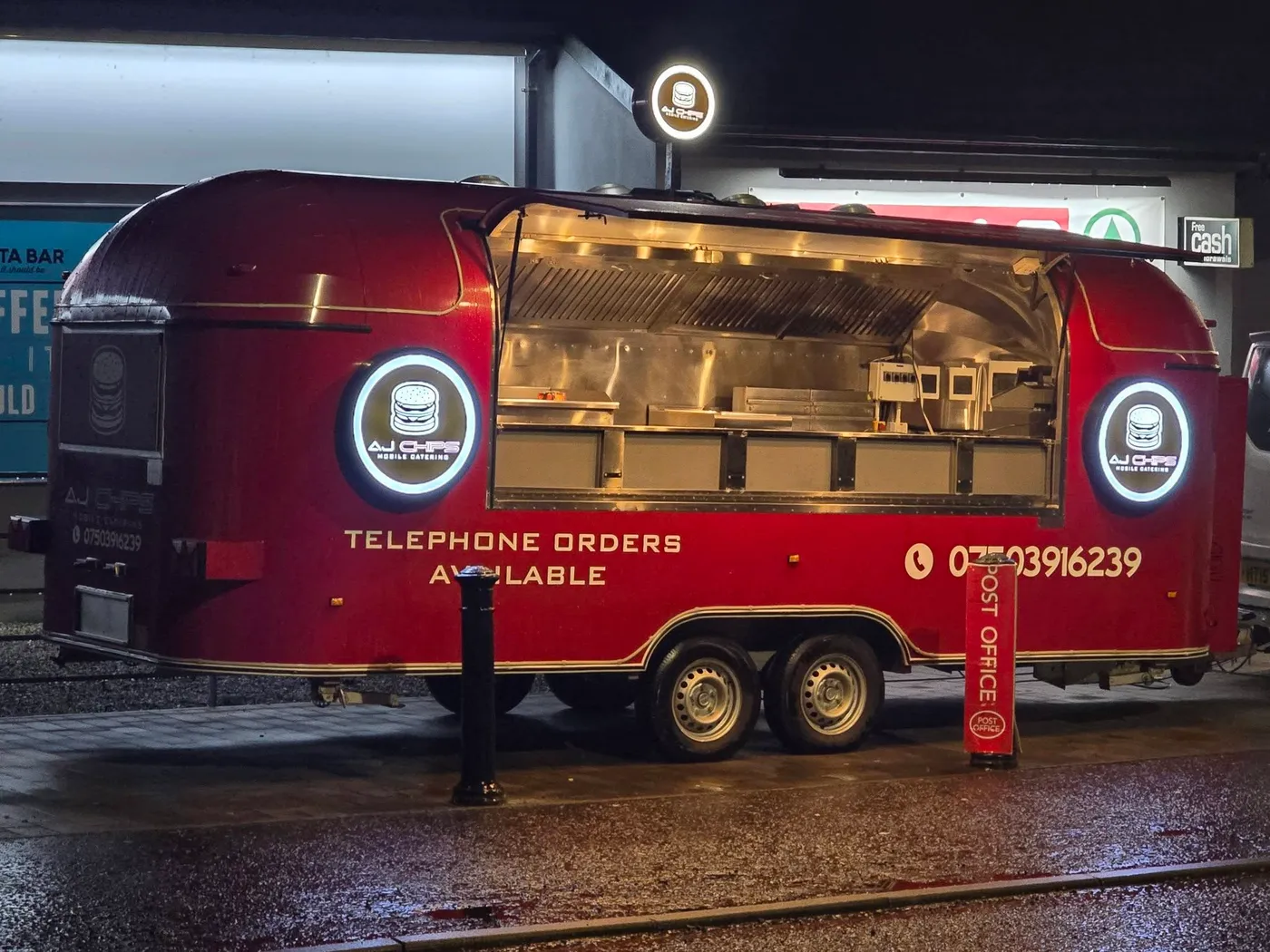 AJ Chips mobile catering trailer at night with illuminated circular logo lightboxes either side of the serving hatch.