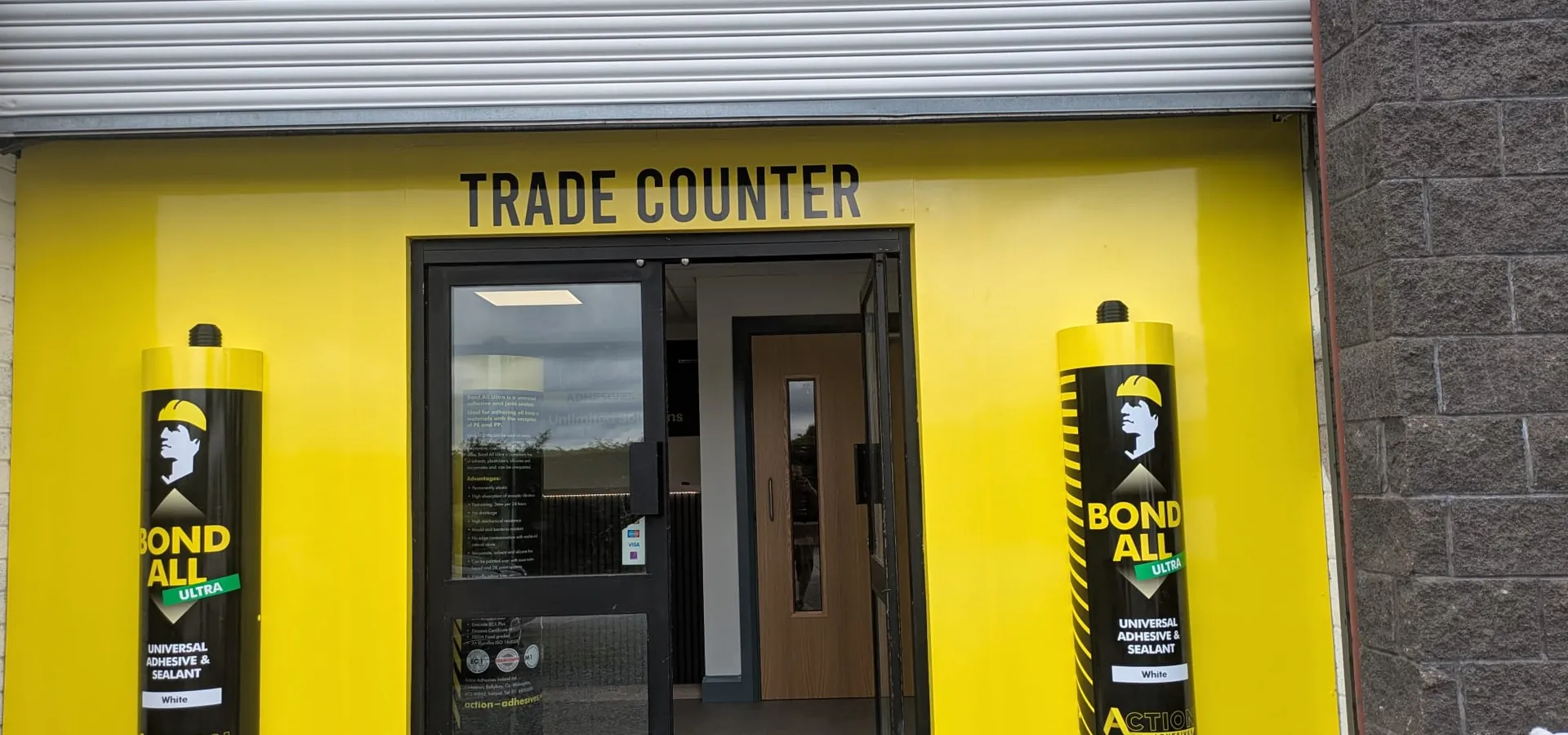 Action Adhesives trade counter shop front in bright yellow with two 5ft replica adhesive tubes flanking the entrance.