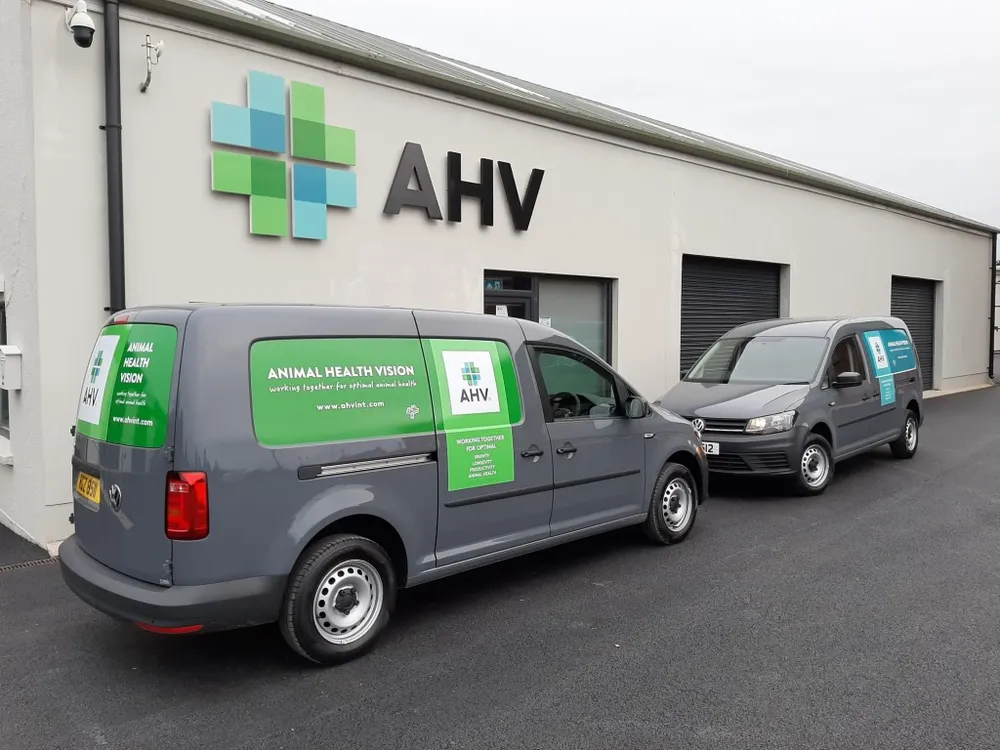 Two Animal Health Vision vans in a branded vinyl wrap, parked outside their premises beneath a dimensional AHV sign.