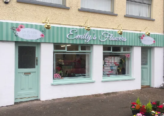 Emily's Flowers shop front with a mint green illuminated fascia sign and hanging light fittings.