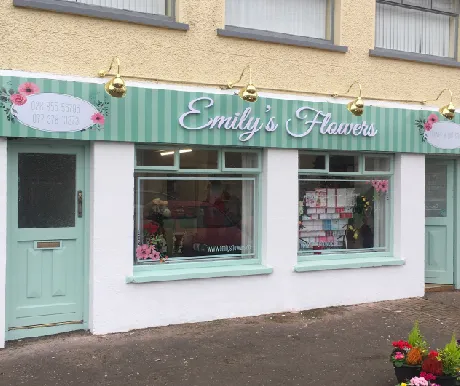 Emily's Flowers shop front with a mint green illuminated fascia sign and hanging light fittings.