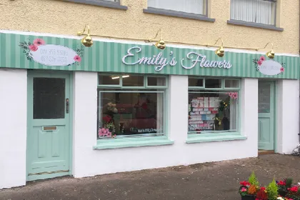 Emily's Flowers shop front with a mint green illuminated fascia sign and hanging light fittings.