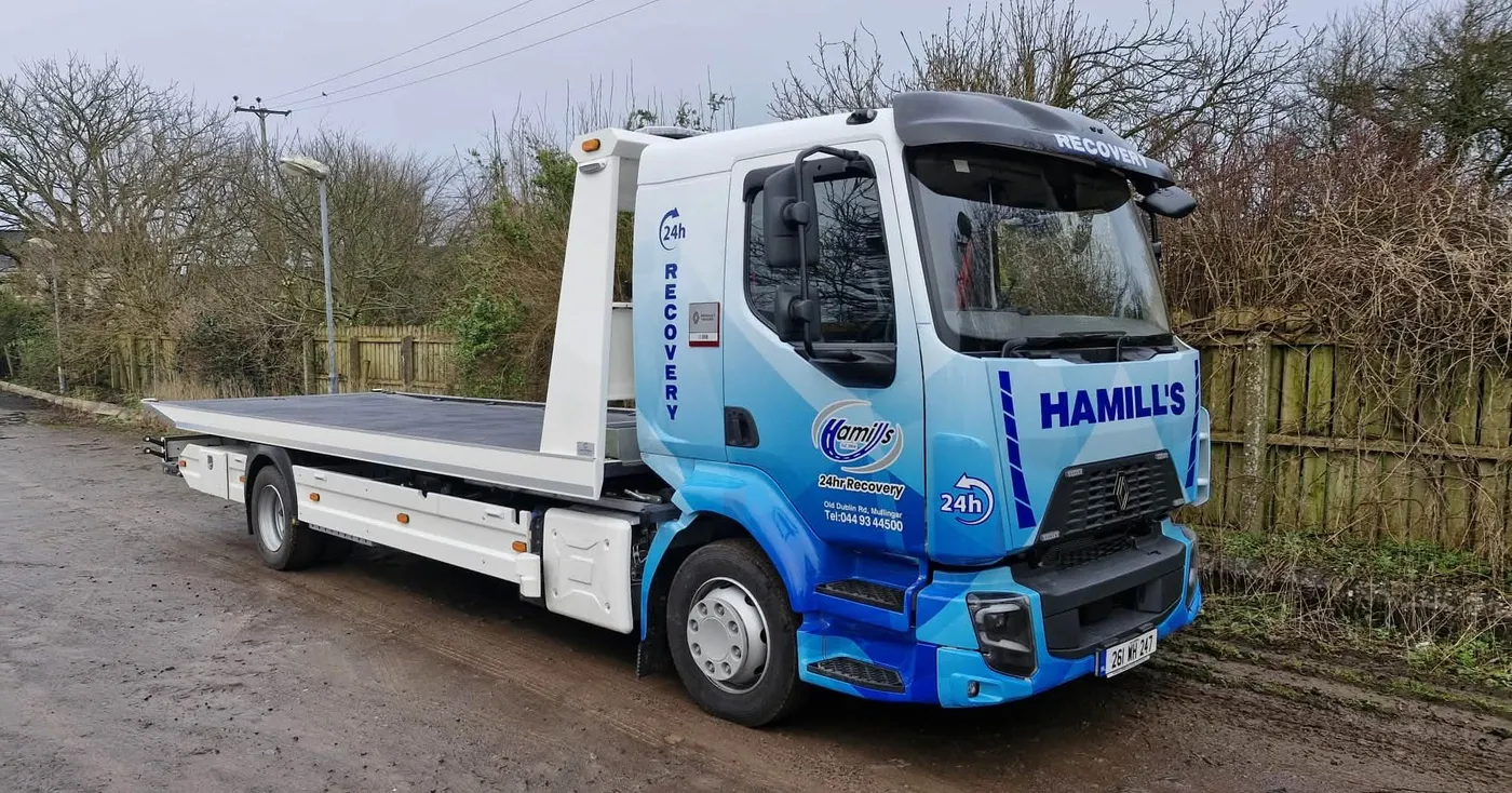 Hamill's 24hr Recovery flatbed truck in a blue geometric vinyl wrap, parked on a rural road.