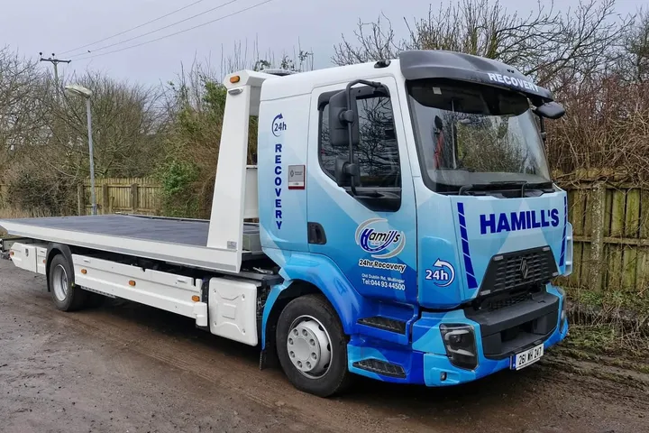 Hamill's 24hr Recovery flatbed truck in a blue geometric vinyl wrap, parked on a rural road.