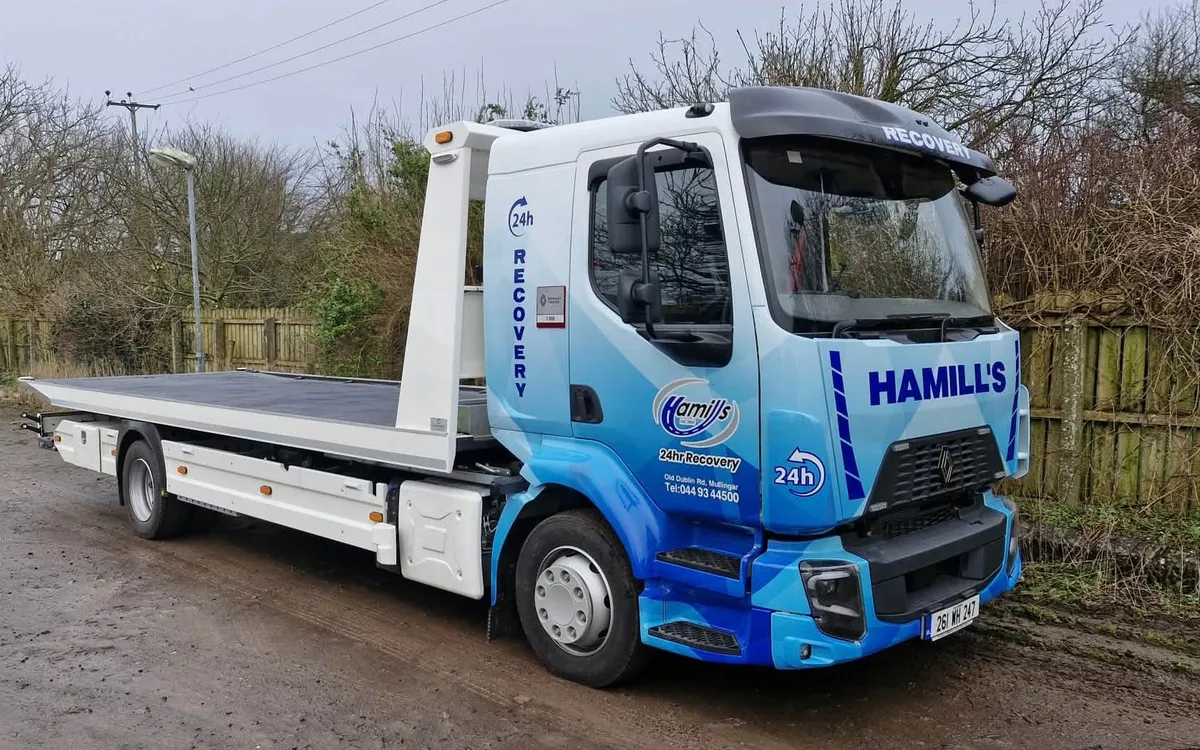 Hamill Group flatbed recovery truck in a blue geometric vinyl wrap, parked on a rural road.
