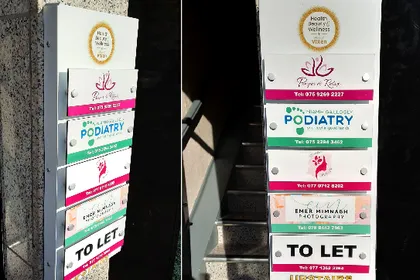 Stacked exterior building directory signs for several tenants, including Flower & Glow and a podiatry clinic.