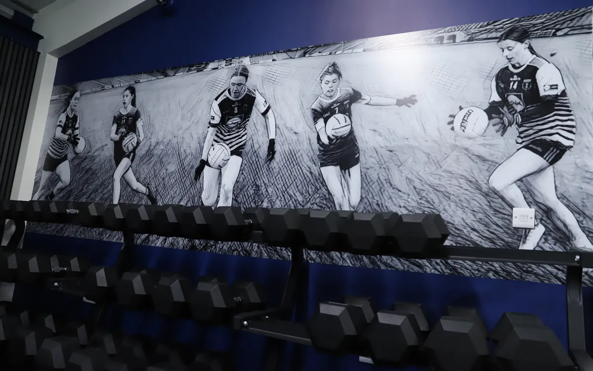 Scotstown GAA gym feature wall showing a black-and-white action sequence of players above a weights rack.