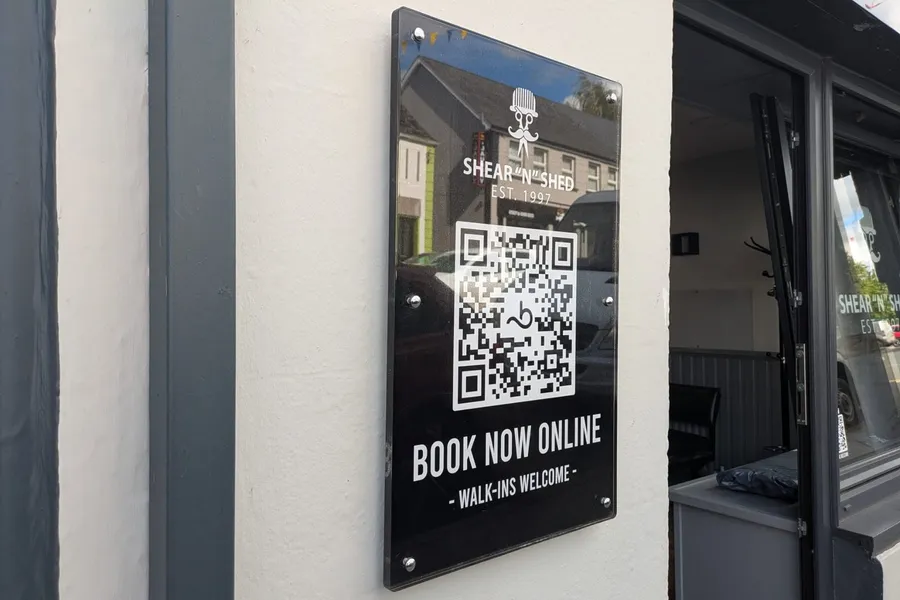 Black acrylic Shear 'n' Shed plaque with gold lettering and a QR code reading Book Now Online.