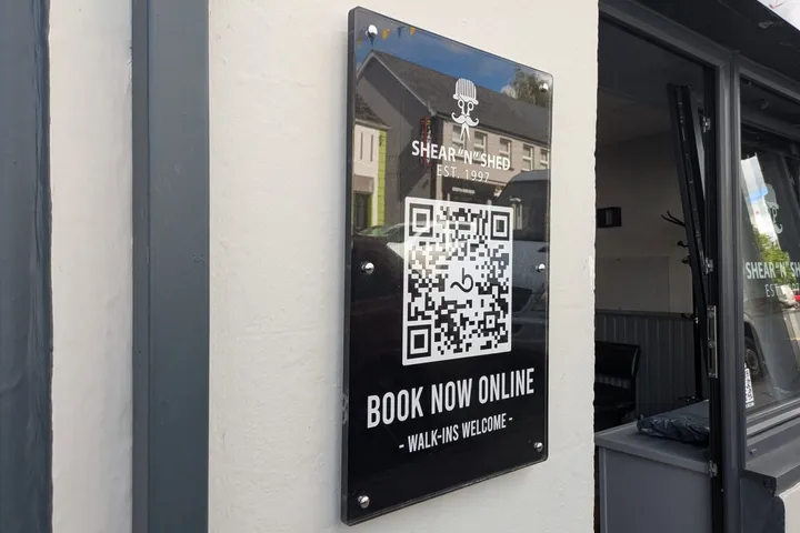 Black acrylic Shear 'n' Shed plaque with gold lettering and a QR code reading Book Now Online.