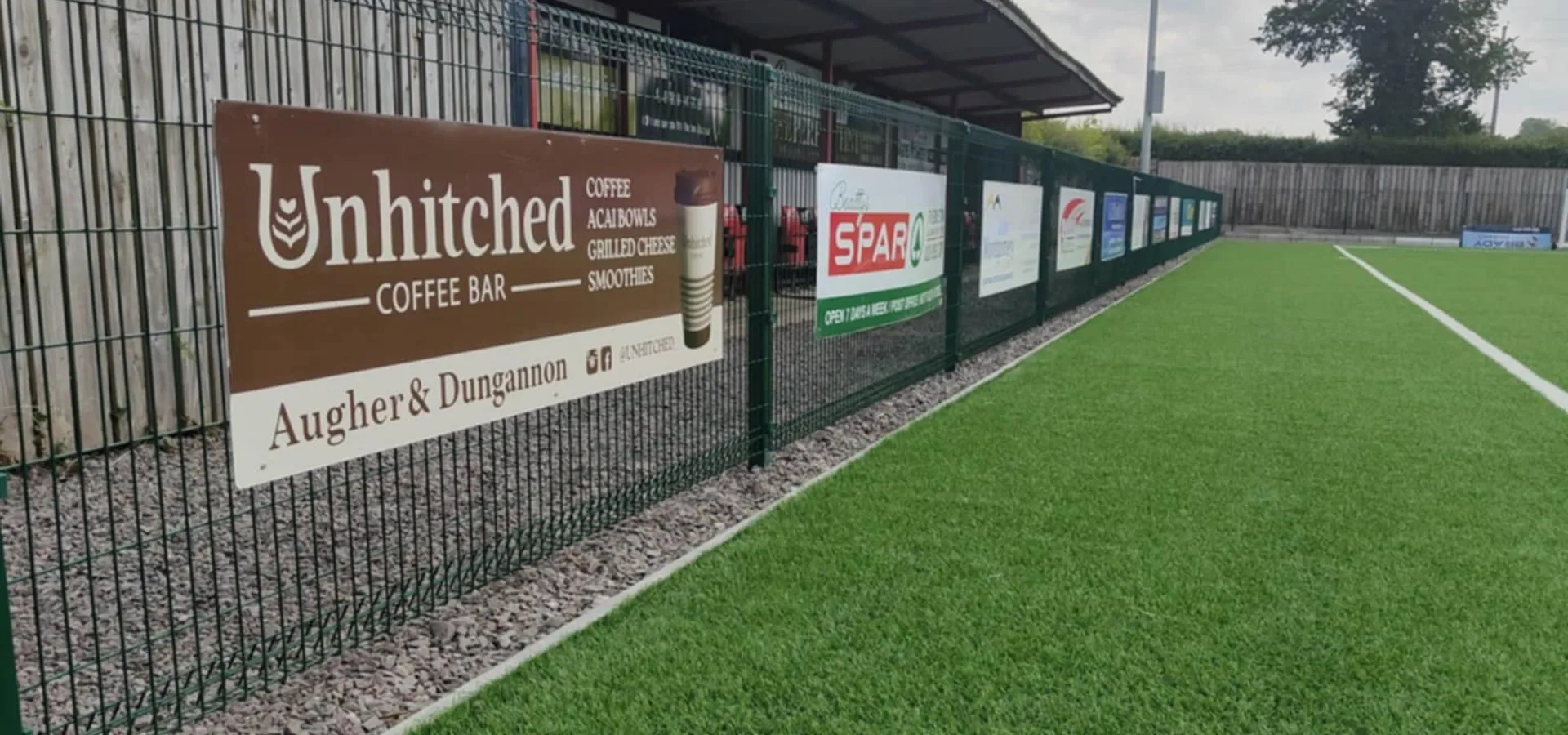 Sponsor advertising boards for local businesses fixed along a sports pitch perimeter fence.