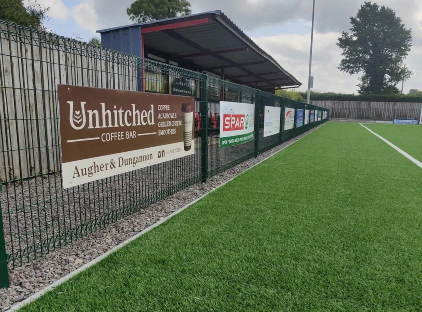 Sponsor advertising boards for local businesses fixed along a sports pitch perimeter fence.