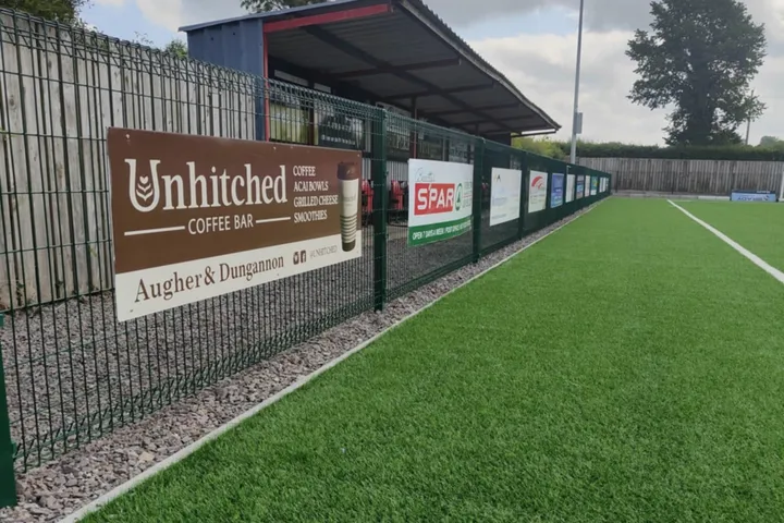 Sponsor advertising boards for local businesses fixed along a sports pitch perimeter fence.