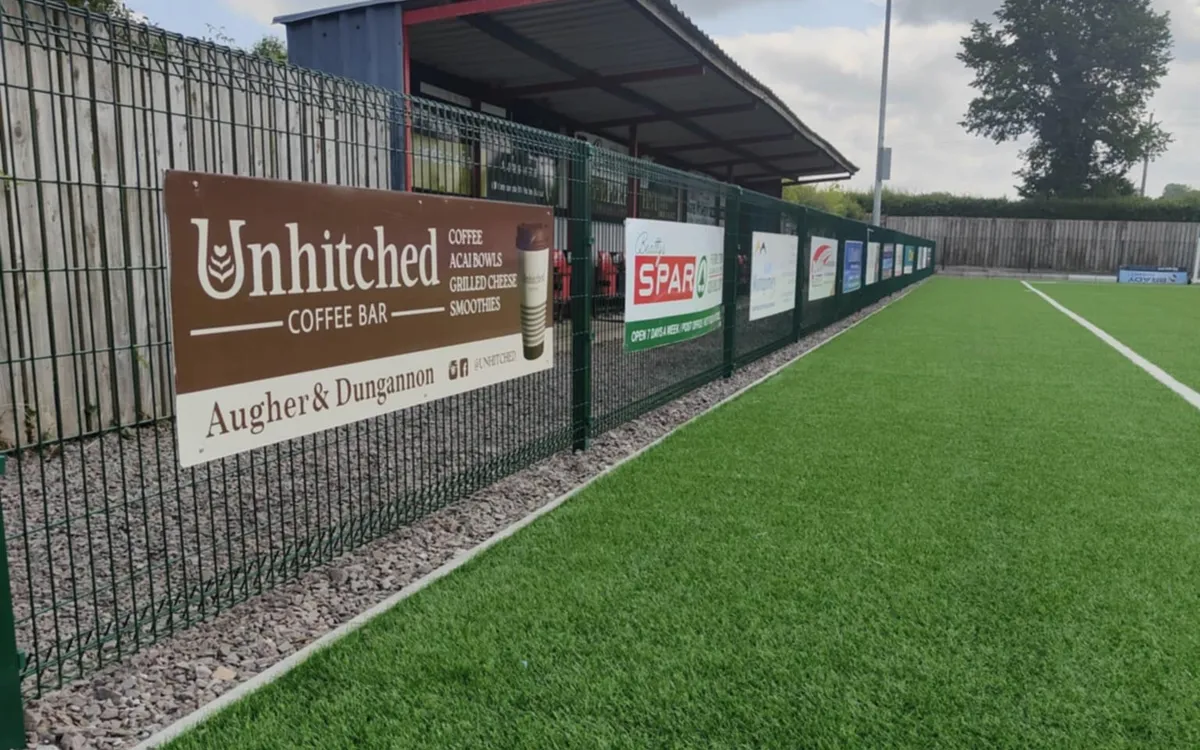 Sponsor advertising boards for local businesses fixed along a sports pitch perimeter fence.