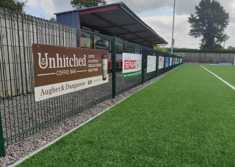 Sponsor advertising boards for local businesses fixed along a sports pitch perimeter fence.